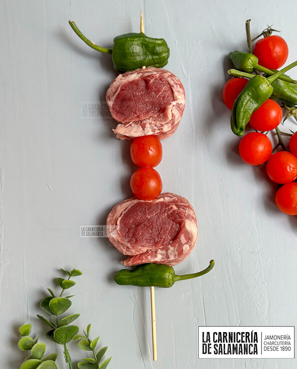 Brocheta de solomillo y secreto ibérico. Además lleva pimientos de padrón y tomates cherry.