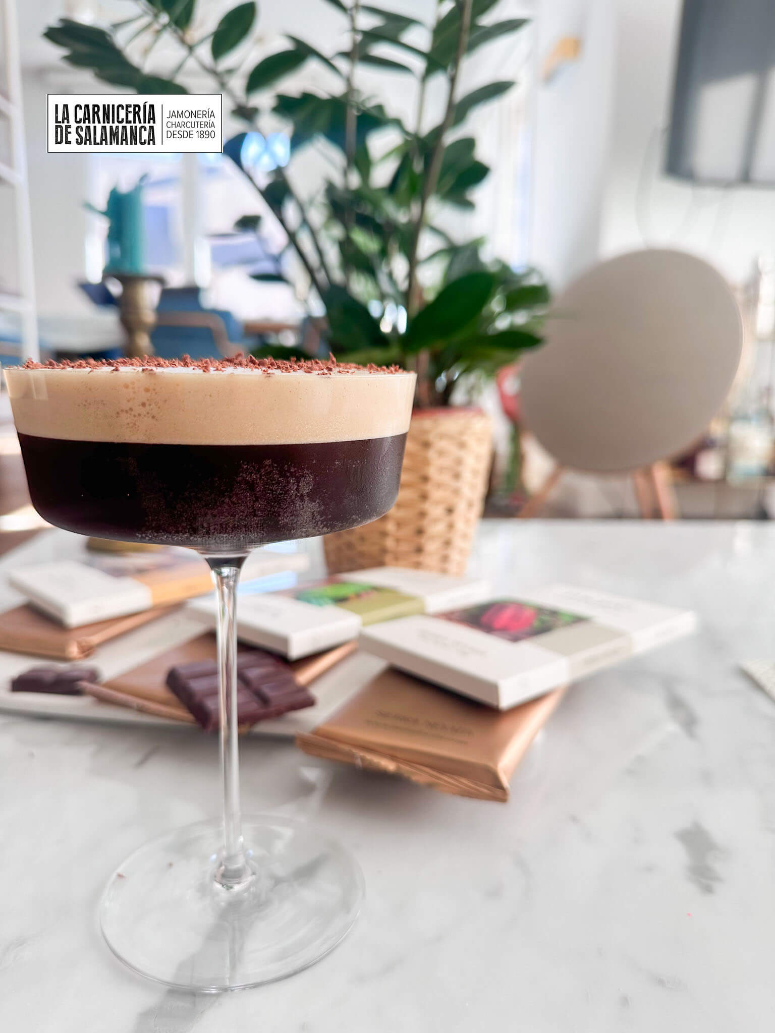 Espresso Martini con virutas de chocolate Moxé ralladas por encima, acompañado de tabletas de chocolate Moxé en un fondo elegante sobre una mesa de mármol.