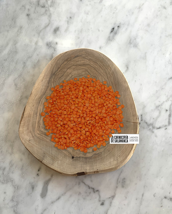 Lentejas coral presentadas en una tabla de madera, disponibles en La Carnicería de Salamanca.