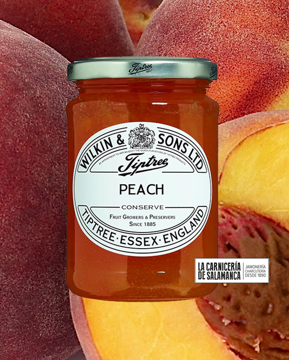 Tarro de mermelada de melocotón Tiptree sobre fondo de melocotones frescos. Producto artesanal sin aditivos, a la venta en La Carnicería de Salamanca, Peñaranda de Bracamonte.